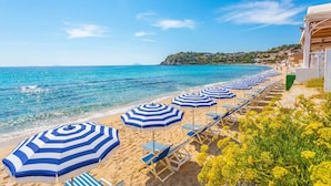 Una playa con sombrillas azul y blanco a rayas, tumbonas y una vista despejada del mar.