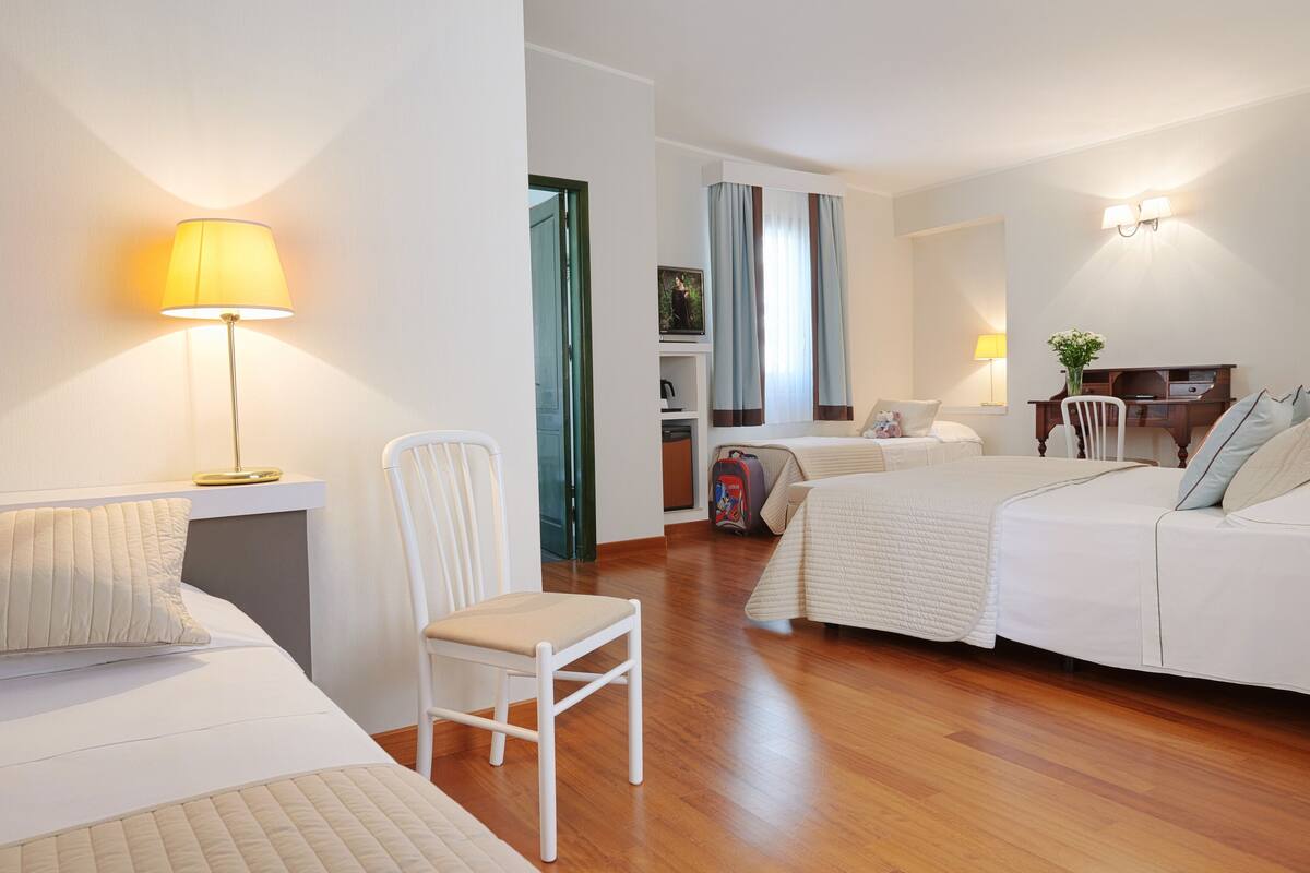 Une chambre d’hôtel avec un lit, une chaise, un bureau, une lampe et une fenêtre avec des rideaux.
