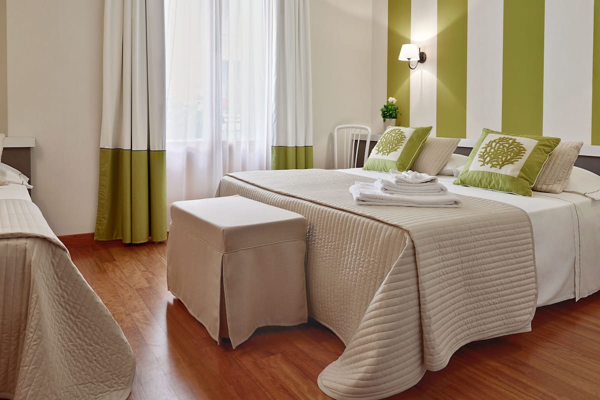 Une chambre d’hôtel avec un lit, une table de chevet, une chaise et une fenêtre avec des rideaux.