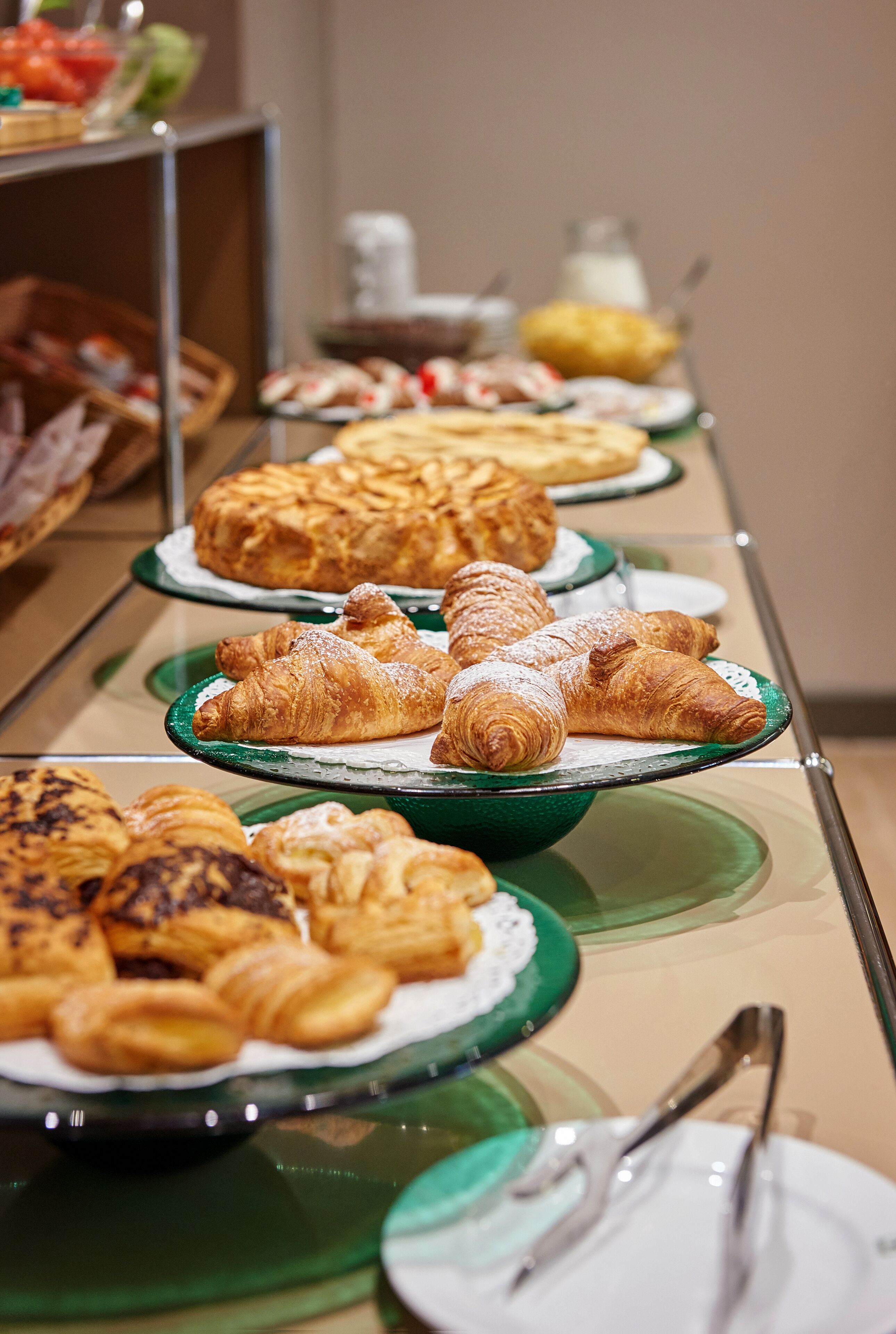 Un bufé con diversas opciones de pastelería y postres en platos de vidrio.