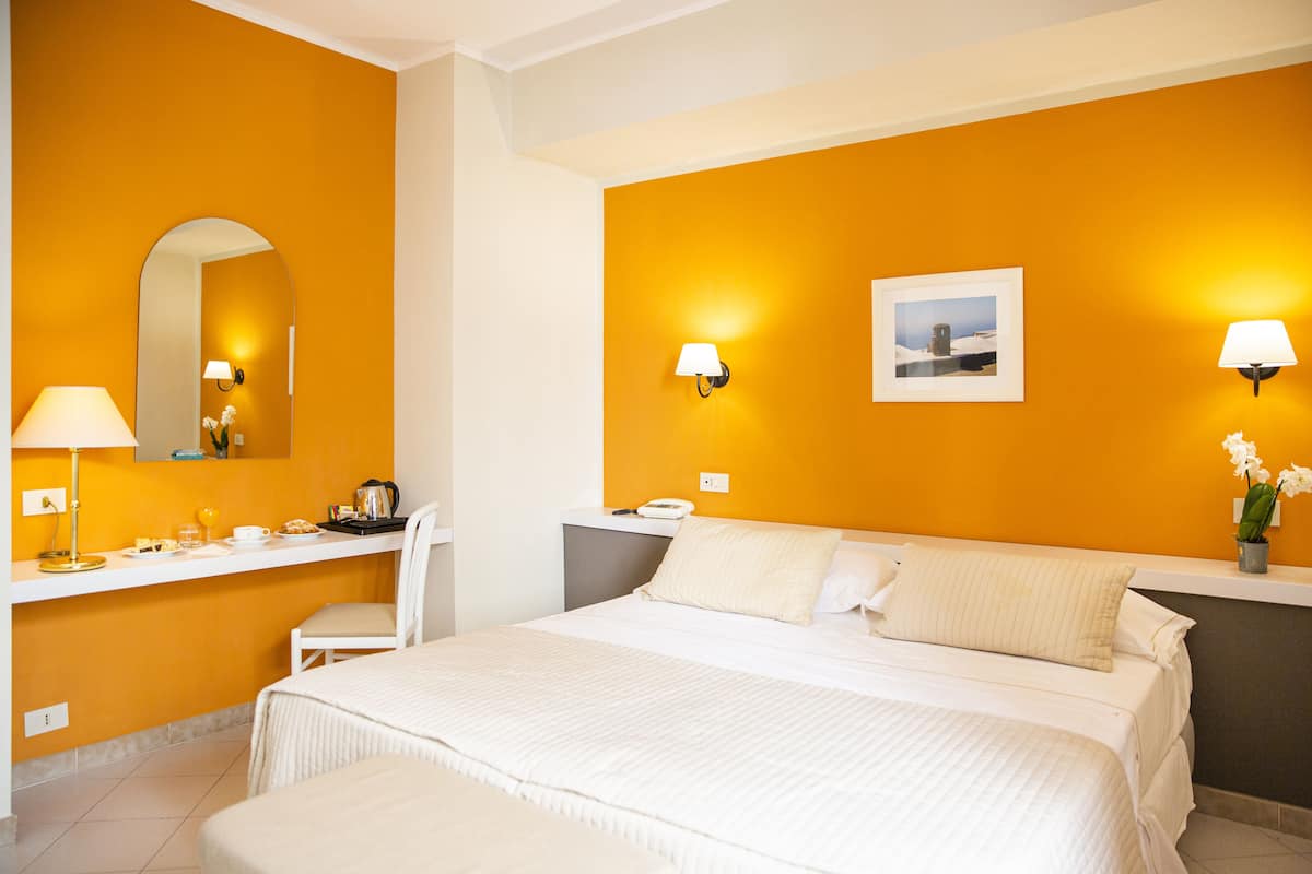 Une chambre d’hôtel avec un grand lit, un bureau avec une lampe, une chaise et une petite table sur laquelle se trouve une cafetière.