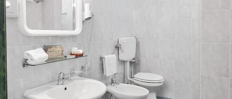 A modern bathroom with two sinks, a toilet, and a glass shelf with toiletries.