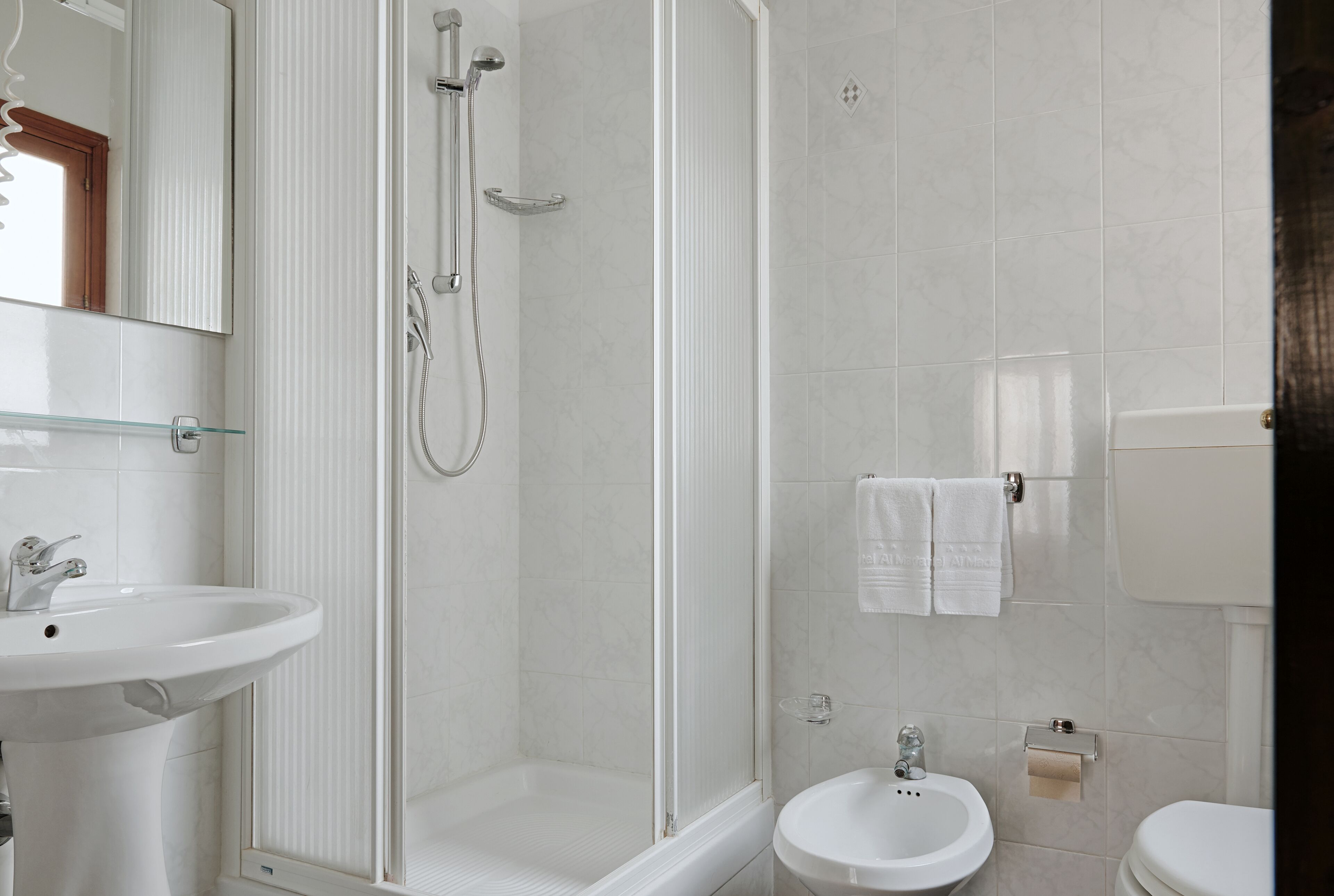 A bathroom with a glass-enclosed shower, a pedestal sink, and a toilet.