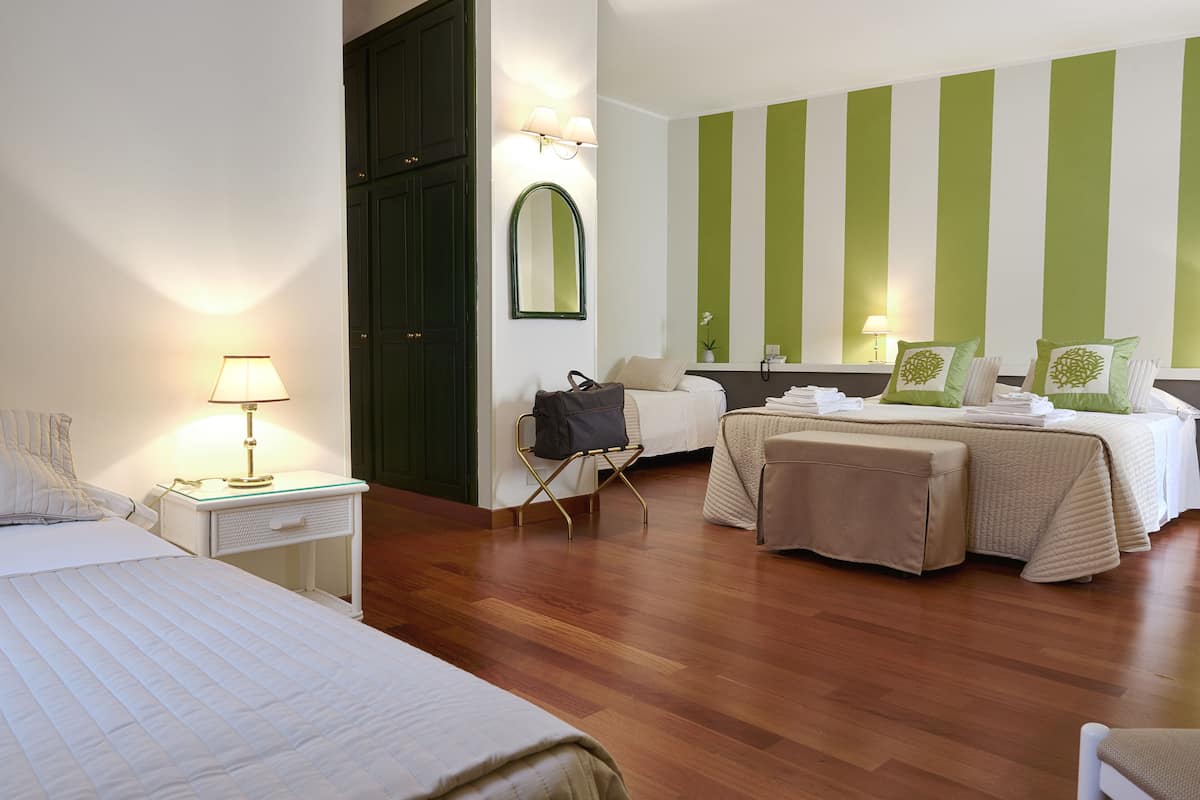 Une chambre d’hôtel avec deux lits, un coin salon, un miroir et un mur à rayures vertes.