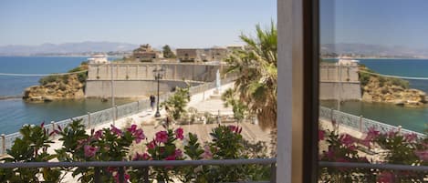 Un balcón con plantas en macetas y vistas a la costa, con edificios y un cielo despejado.