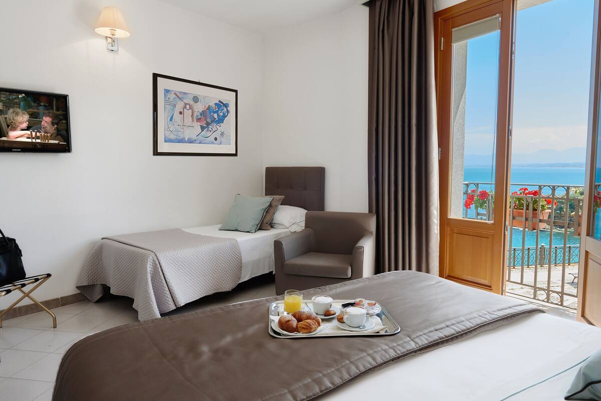 Une chambre d’hôtel comprenant un lit, une chaise, un bureau, une télévision et un balcon avec vue sur la piscine.