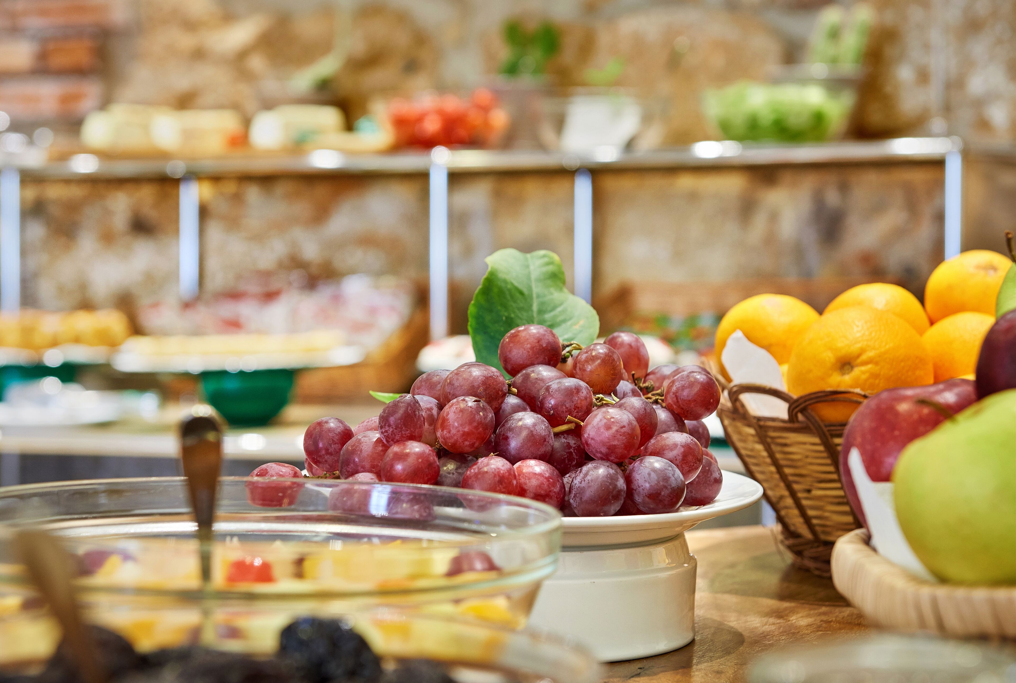 A buffet with various fruits and desserts, including grapes, oranges, and a bowl of mixed berries.