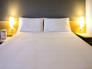 Ein Hotelzimmer mit einem großen Bett, zwei Nachttischlampen und einem Nachttisch mit einer Speisekarte.