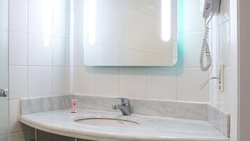 A bathroom with a white tiled wall, a large mirror, a white sink, and a hairdryer on the wall.