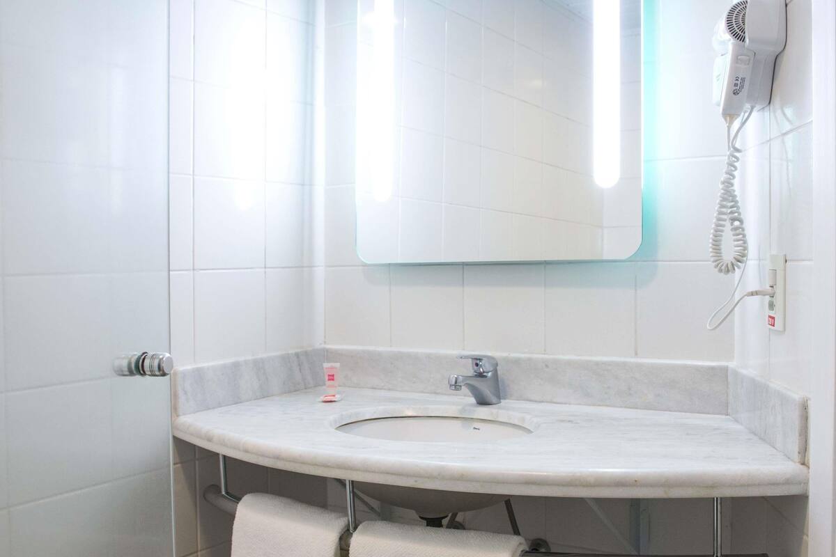 A bathroom with a white sink, a mirror, and a hairdryer mounted on the wall.