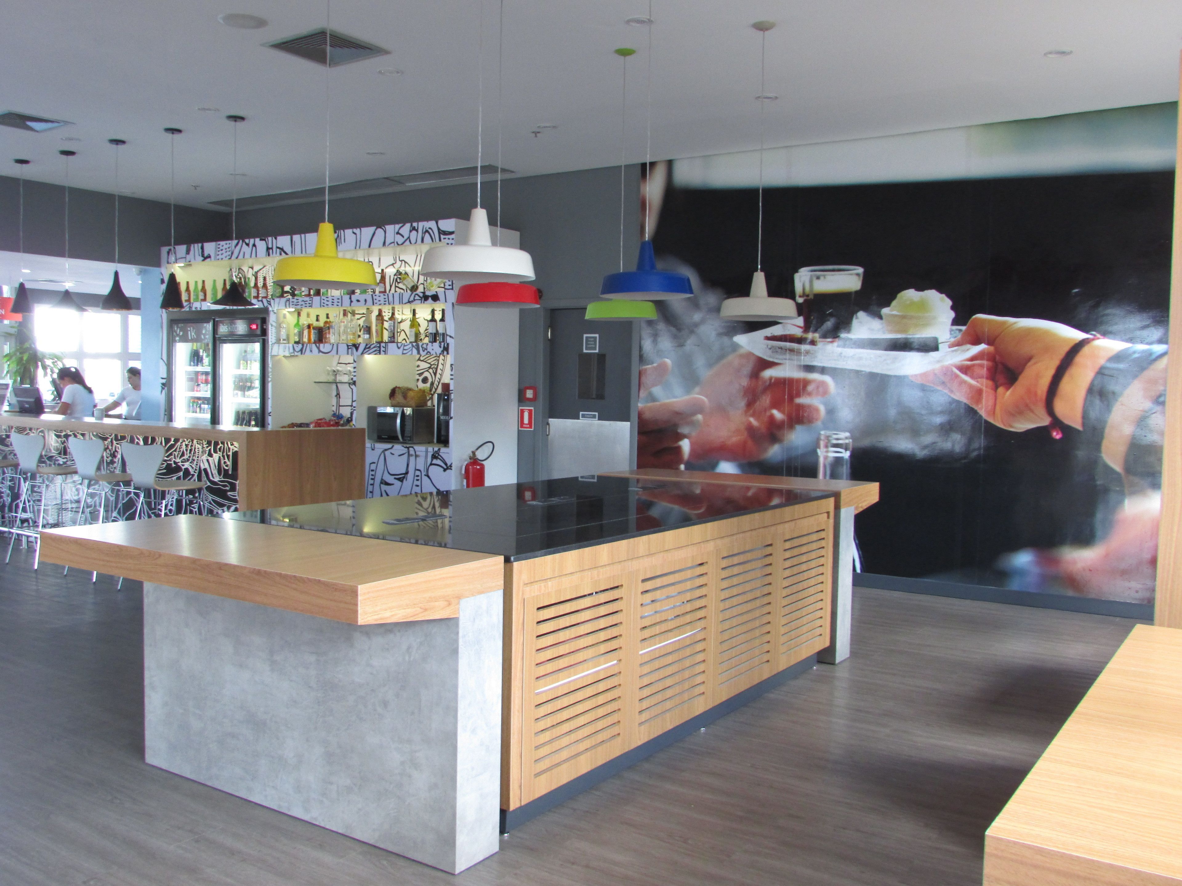 A modern bar area with a central counter, hanging pendant lights, and a mural depicting a hand holding a tray.