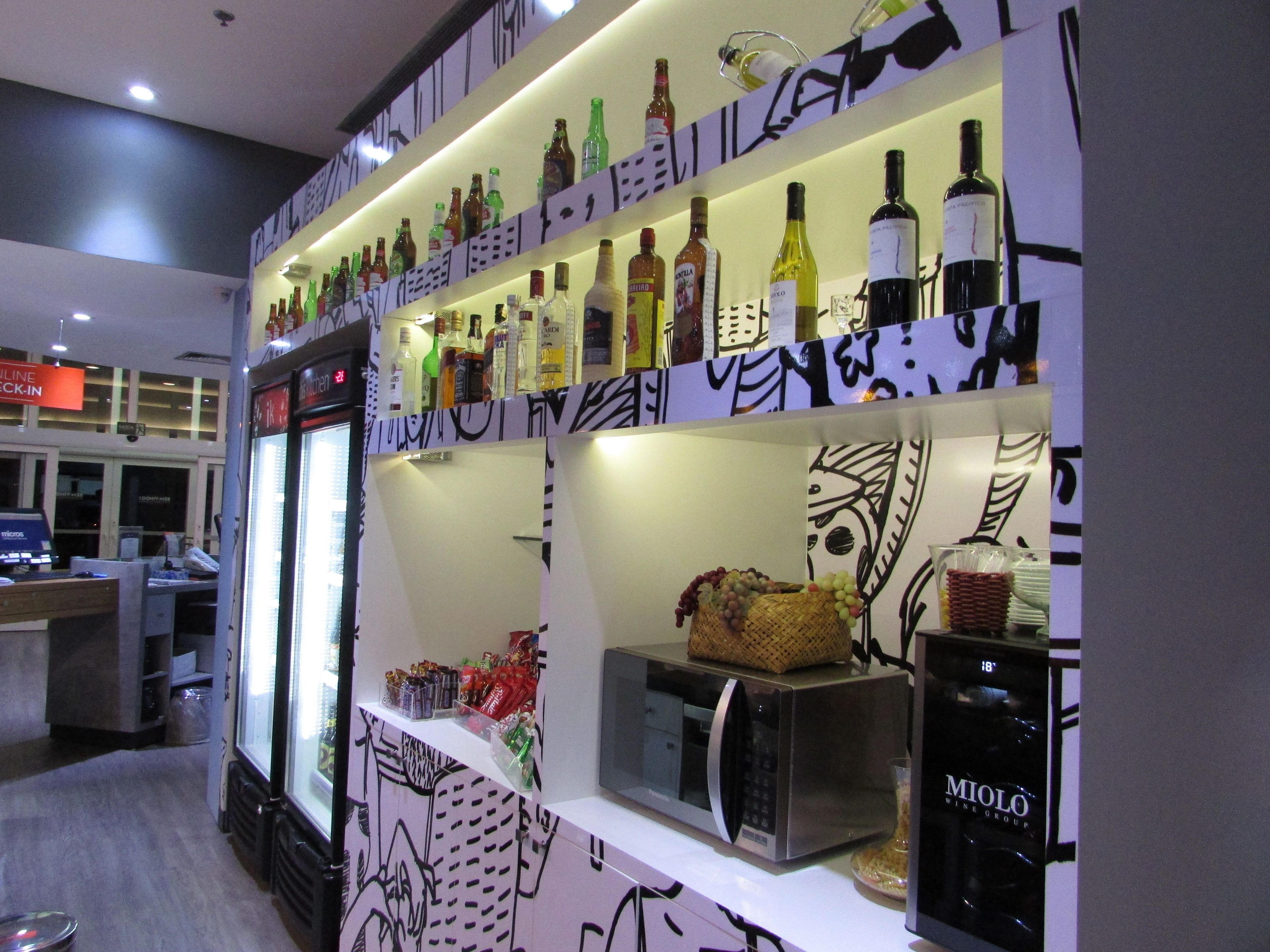 Uma área de bar com prateleiras cheias de garrafas de bebidas, um micro-ondas e uma cesta de uvas.