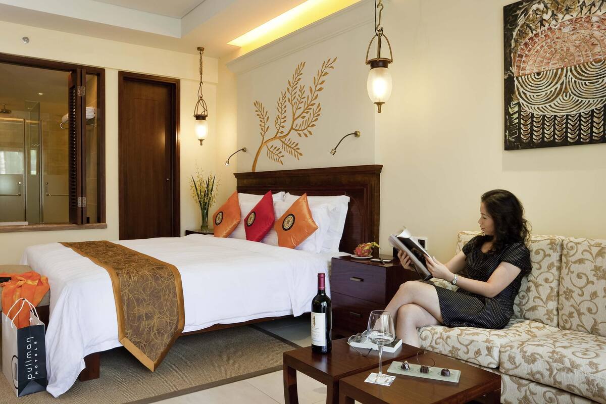 A hotel room with a bed, a sofa, a coffee table, and a wall with a decorative piece.