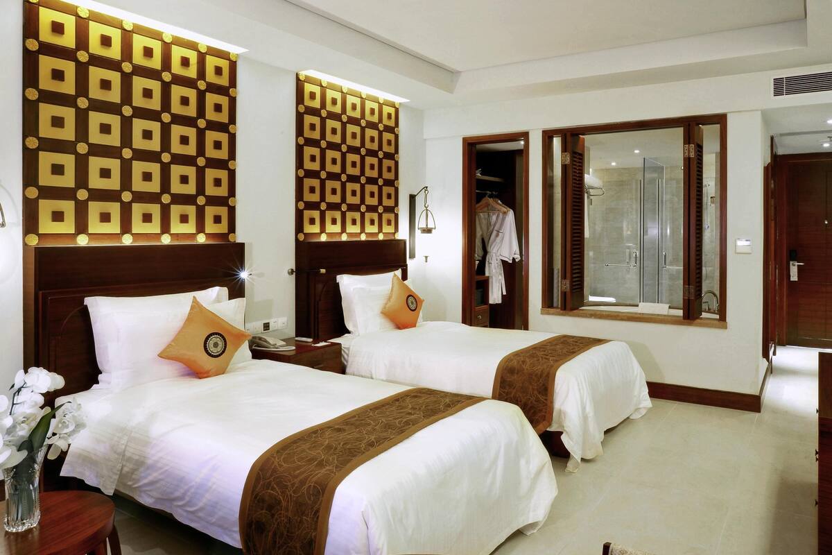 A hotel room with two beds, a bathroom with a glass shower, and a wardrobe.