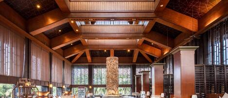 A spacious lobby with high ceilings, wooden beams, and a central column. There are seating areas with cushioned chairs and a bar area with a counter.