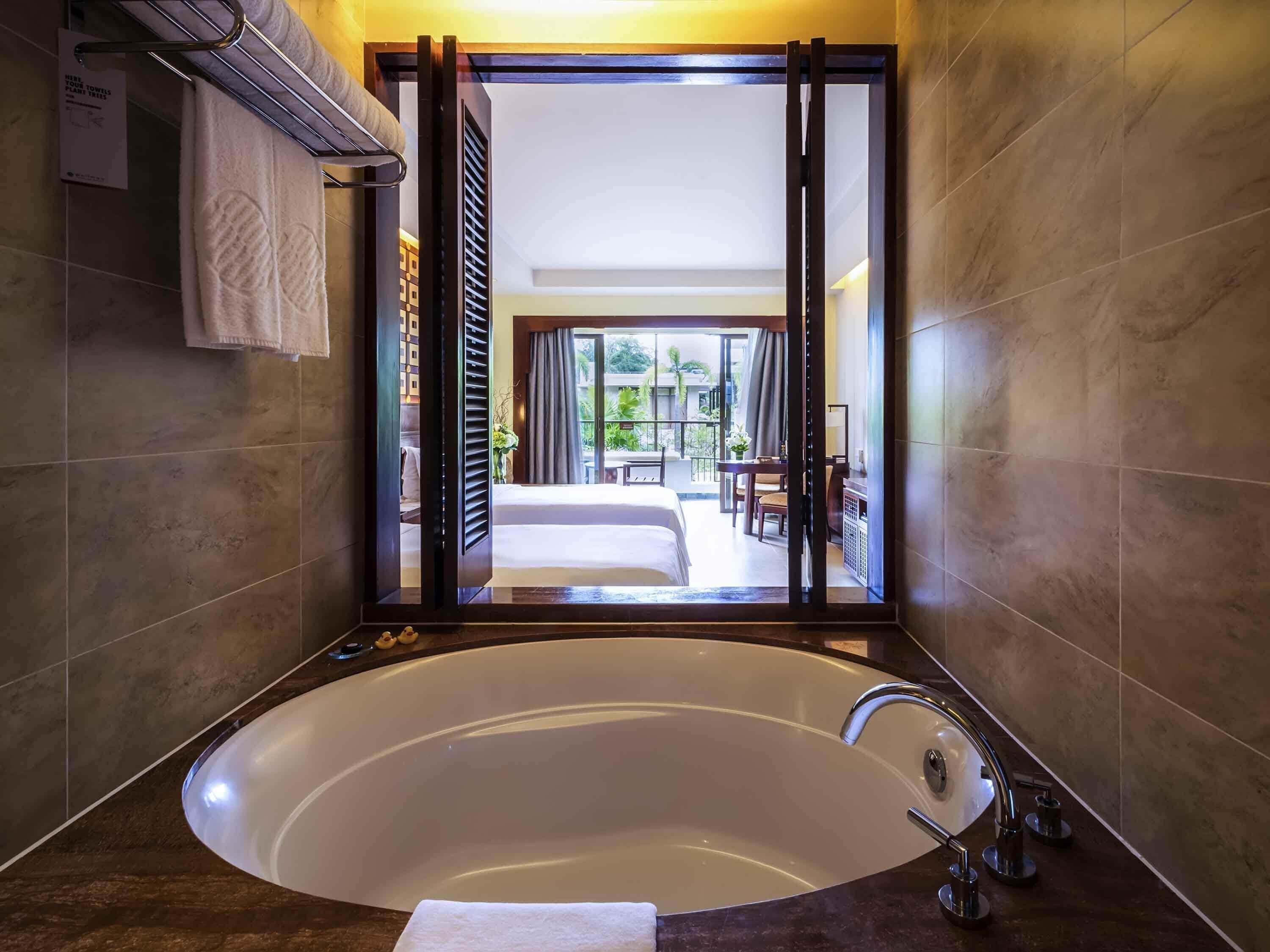 Un baño moderno con una bañera grande, un perchero y vistas a un dormitorio y un balcón.