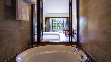 A modern bathroom with a large bathtub, a towel rack, and a view of a bedroom and balcony.
