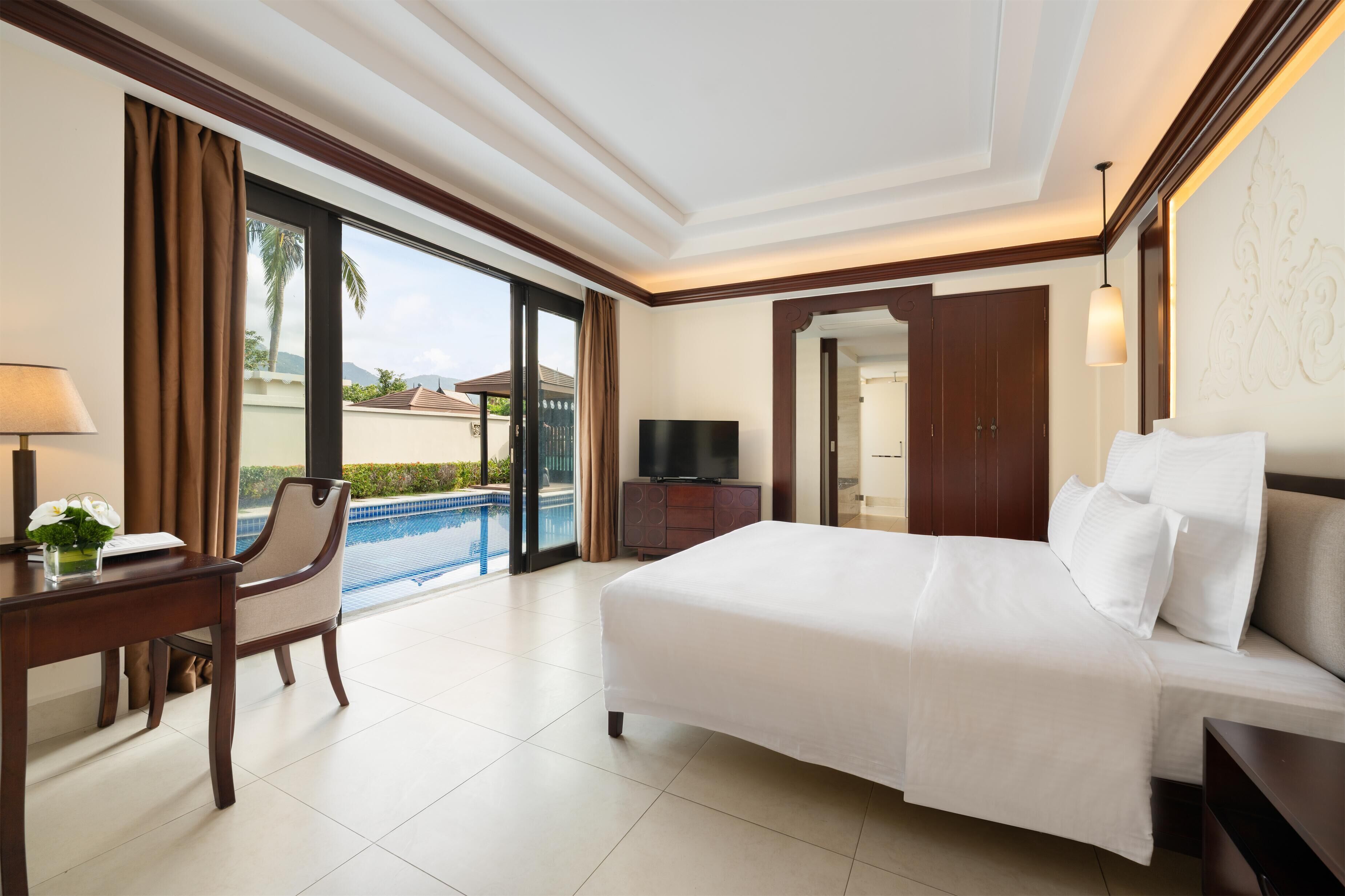 A hotel room with a bed, a desk, a chair, a TV, and a view of a swimming pool.