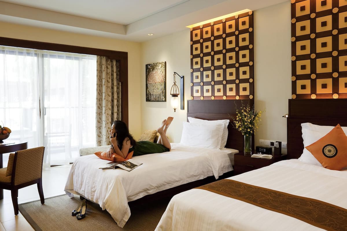A hotel room with two beds, a desk, a chair, and a large window with curtains.