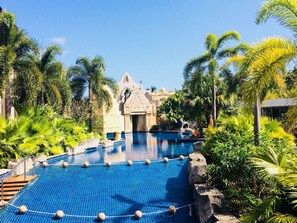 A large outdoor swimming pool surrounded by palm trees and a stone building with a pointed roof.