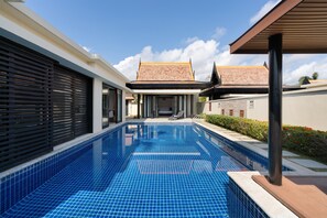 A swimming pool with a tiled deck, adjacent to a building with a modern design and a traditional roof.