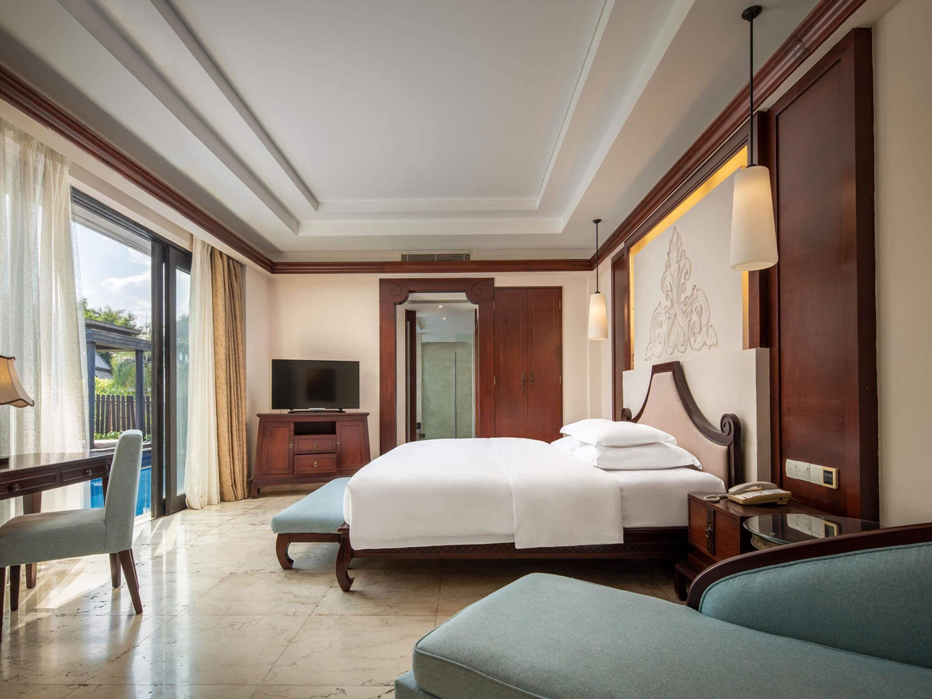 Quarto de hotel com cama, escrivaninha, cadeira, televisão e vista para o exterior.