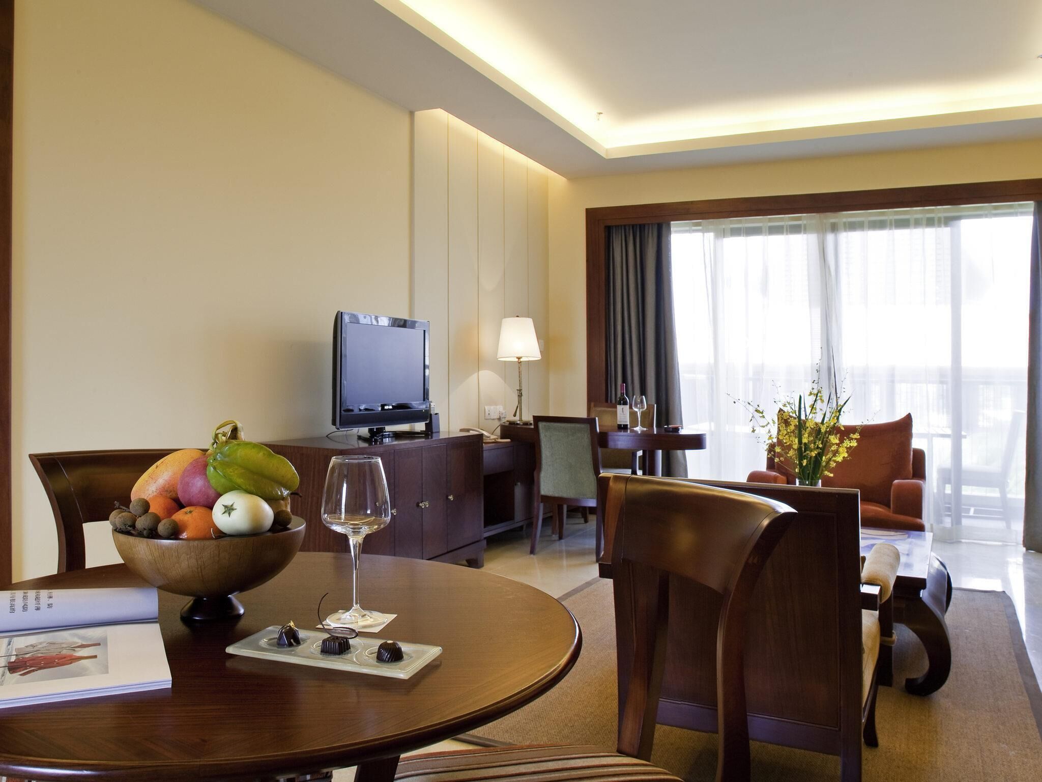 Habitación de hotel con una mesa de comedor, sillas, televisor, sofá y una ventana con cortinas.