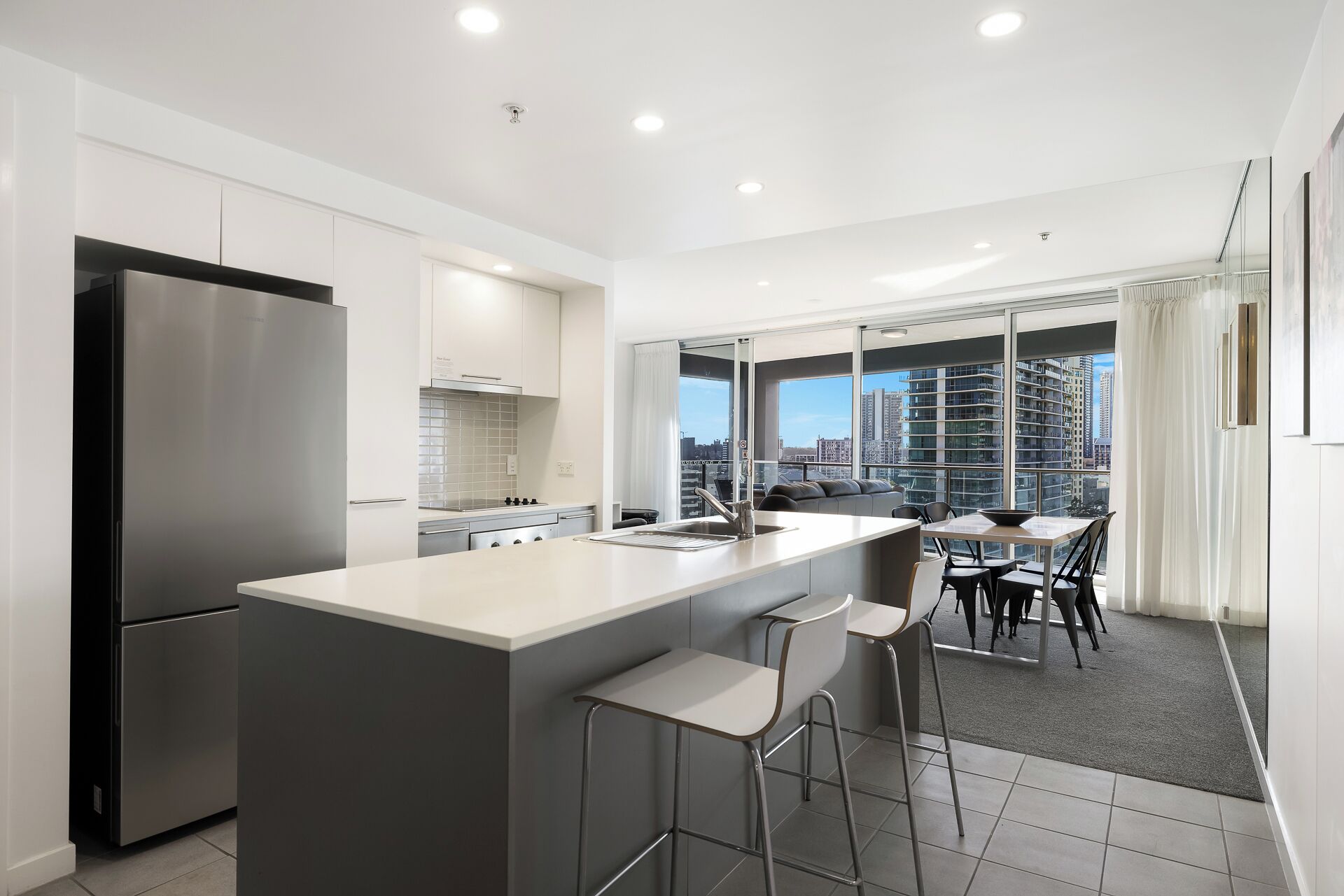 A modern kitchen with a central island, stainless steel appliances, and a dining area with a view of the city.