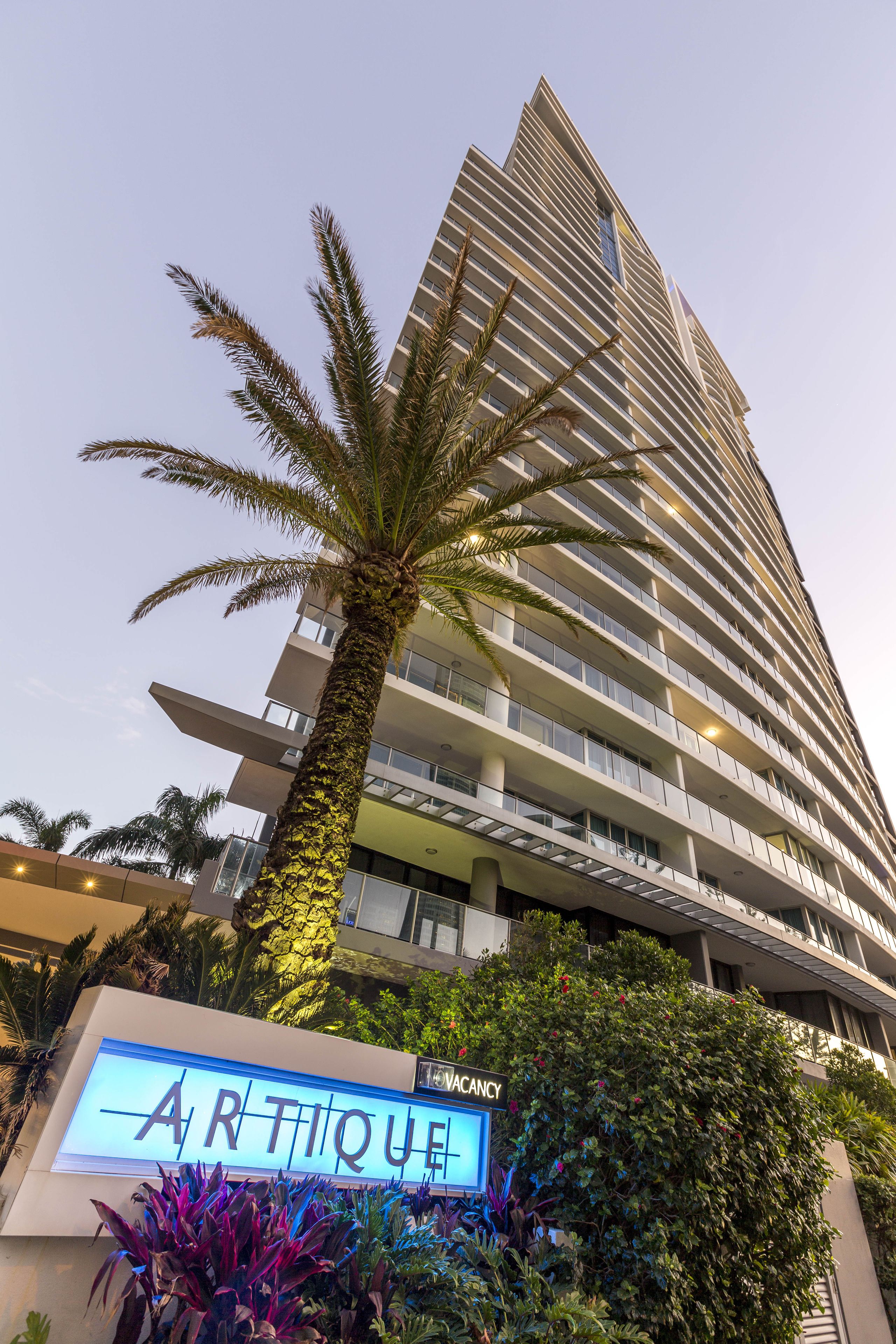 Un edificio alto con un letrero que dice "ARTIQUE" y una palmera frente a él.