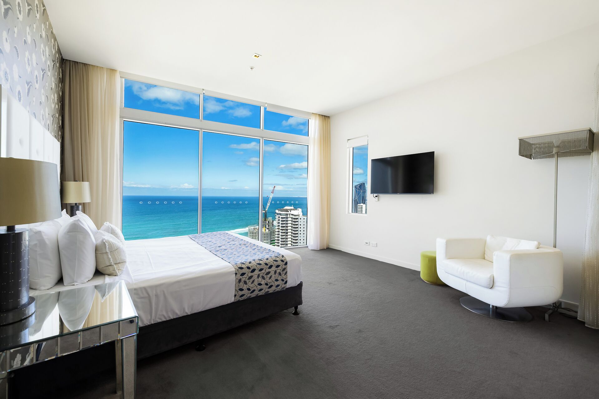A hotel room with a large bed, a TV, a desk, and a view of the ocean.