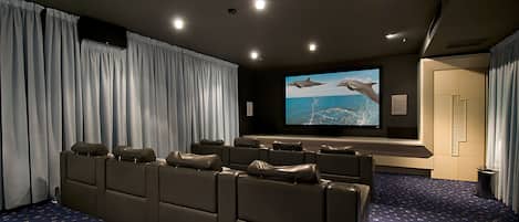 A home theater with a large screen, reclining seats, and a carpeted floor.