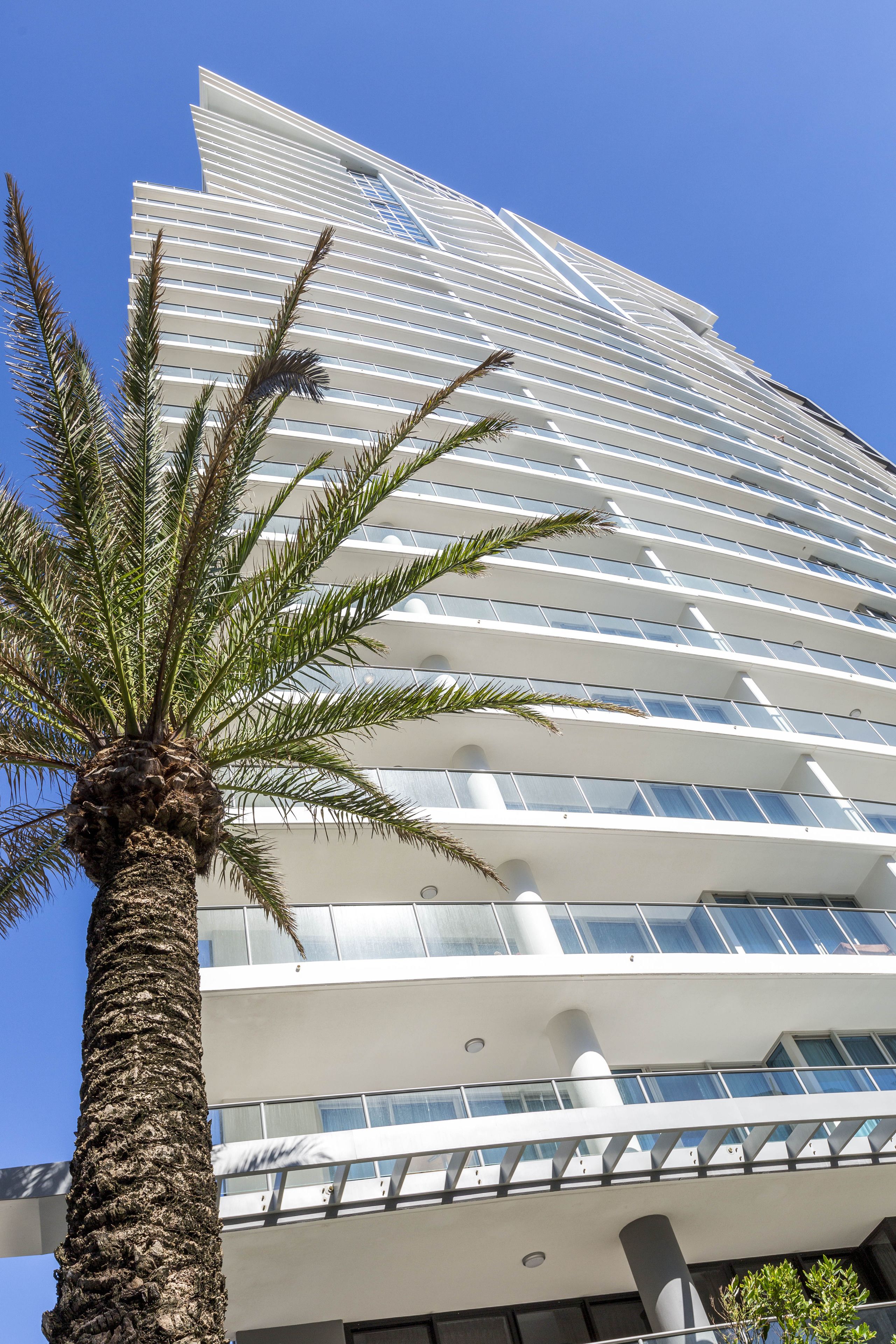 A tall, modern building with multiple balconies and a palm tree in the foreground.