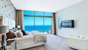 Ein modernes Schlafzimmer mit großem Fenster und Meerblick, ein Bett, ein Fernseher und eine Sitzecke.