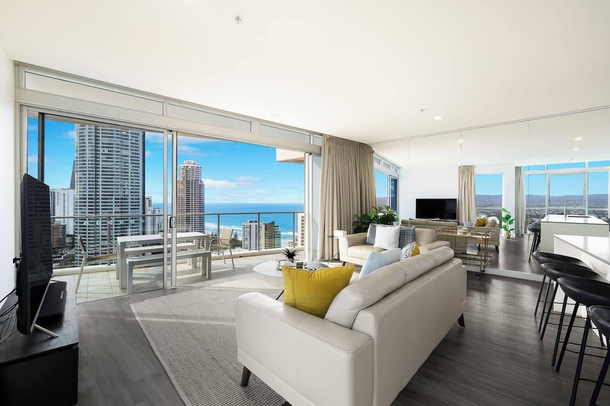 Een moderne woonkamer met een grote bank, een eethoek en een balkon met uitzicht over de stad.