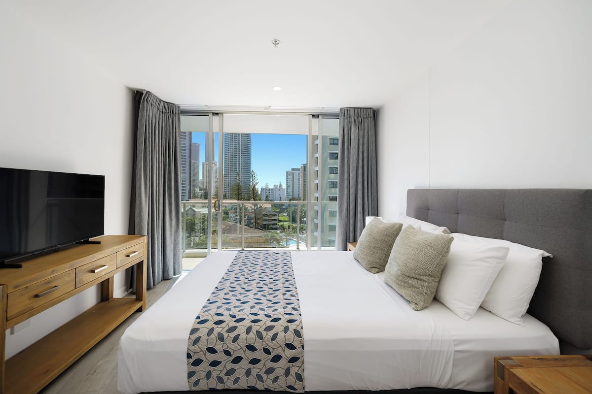 Een moderne hotelkamer met een groot bed, een televisie en een balkon met uitzicht op de stad.
