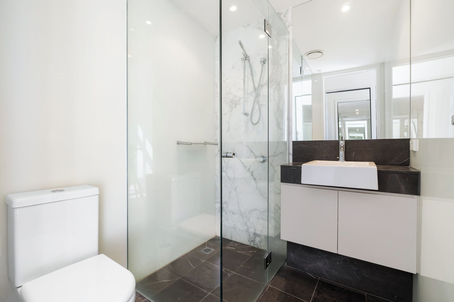 A modern bathroom with a glass-enclosed shower, a white toilet, and a vanity with a black countertop.