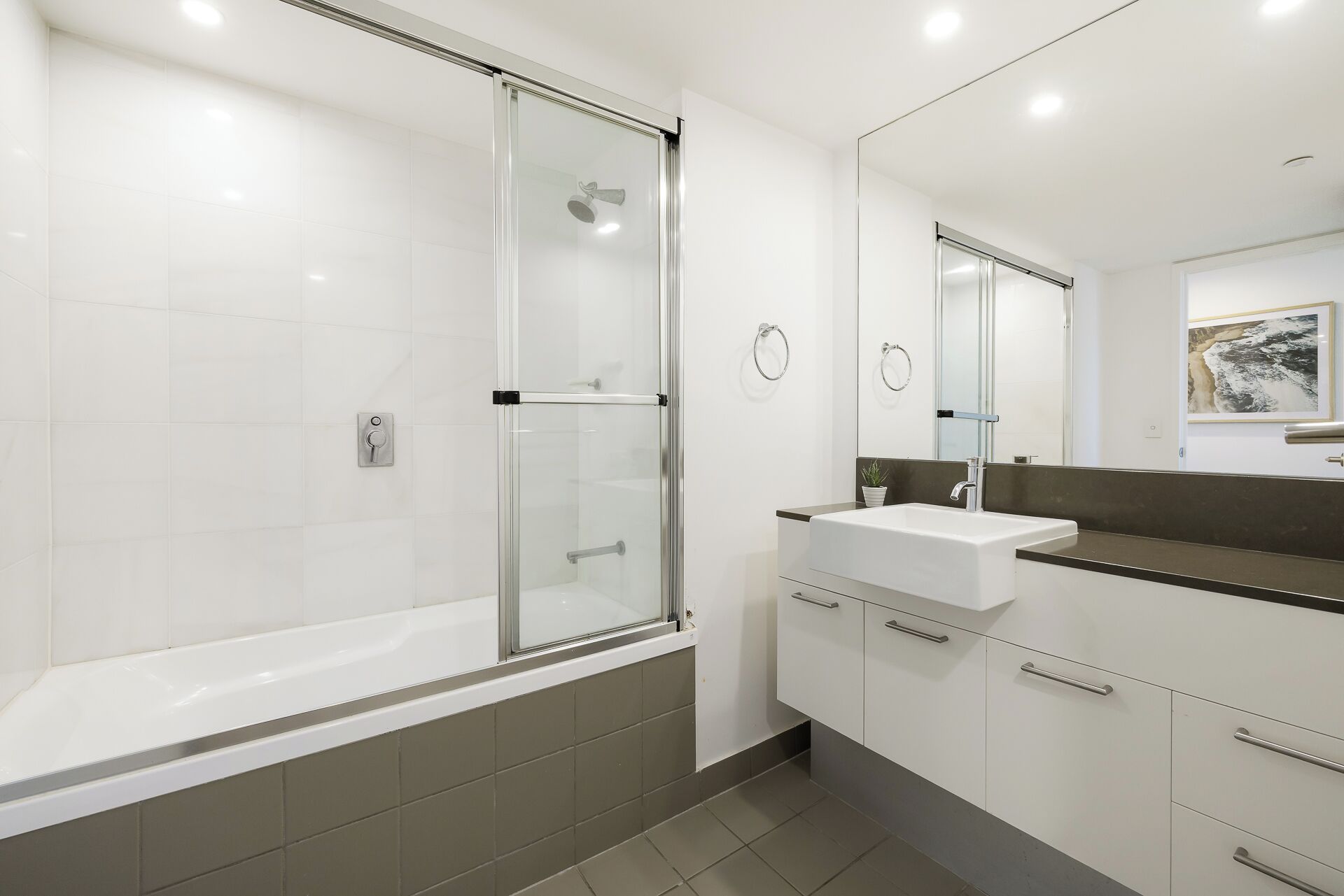 A modern bathroom with a glass-enclosed shower, a white sink, and a dark countertop.