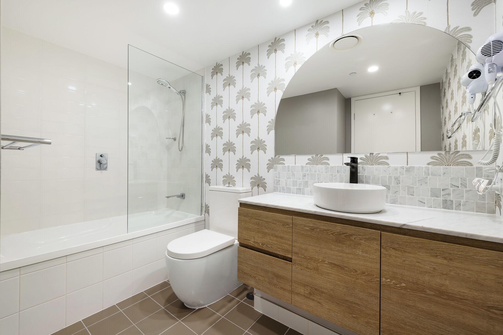A modern bathroom with a glass shower enclosure, a white toilet, and a vanity with a wooden cabinet and a white sink.