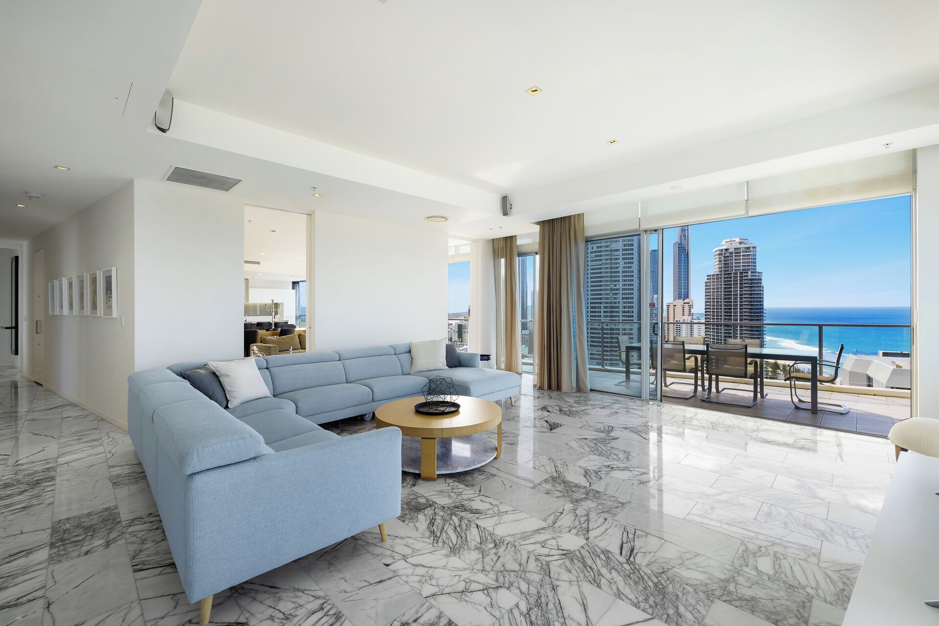 A modern living room with a sectional sofa, a round coffee table, and a view of the ocean and city skyline.
