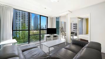Una sala de estar moderna con un ventanal grande, un televisor de pantalla plana, un sofá, una mesa de centro y un balcón con una silla.