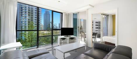 A modern living room with a large window, a flat-screen TV, a sofa, a coffee table, and a balcony with a chair.