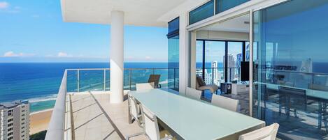 A balcony with a table and chairs, overlooking a beach and city skyline.