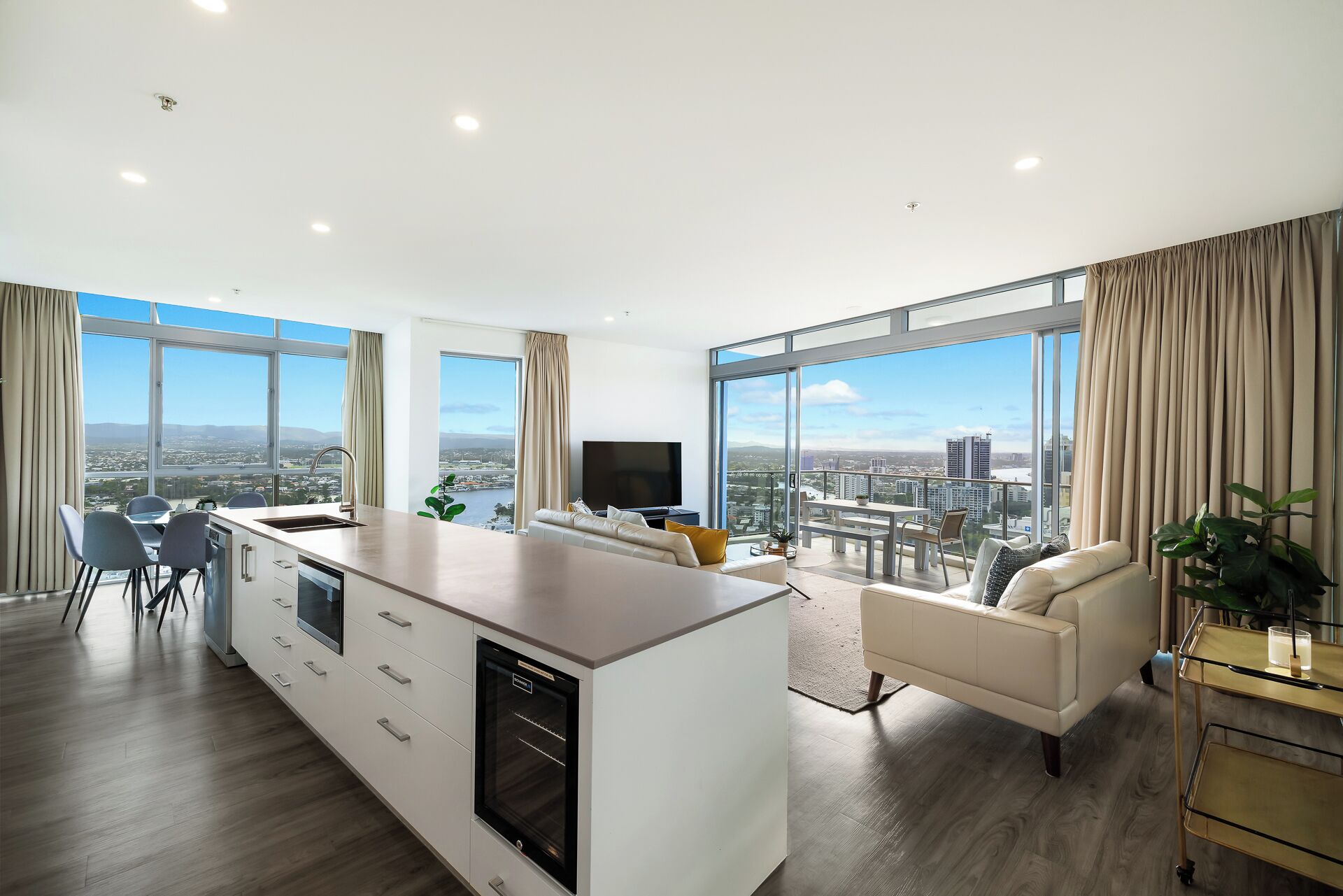 A modern living room with a kitchen area, large windows, and a city view.