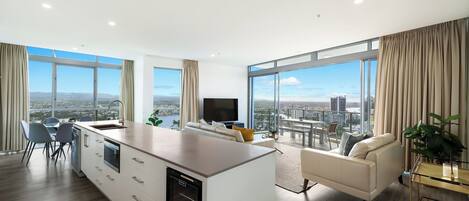 A modern living room with a kitchen area, large windows, and a city view.