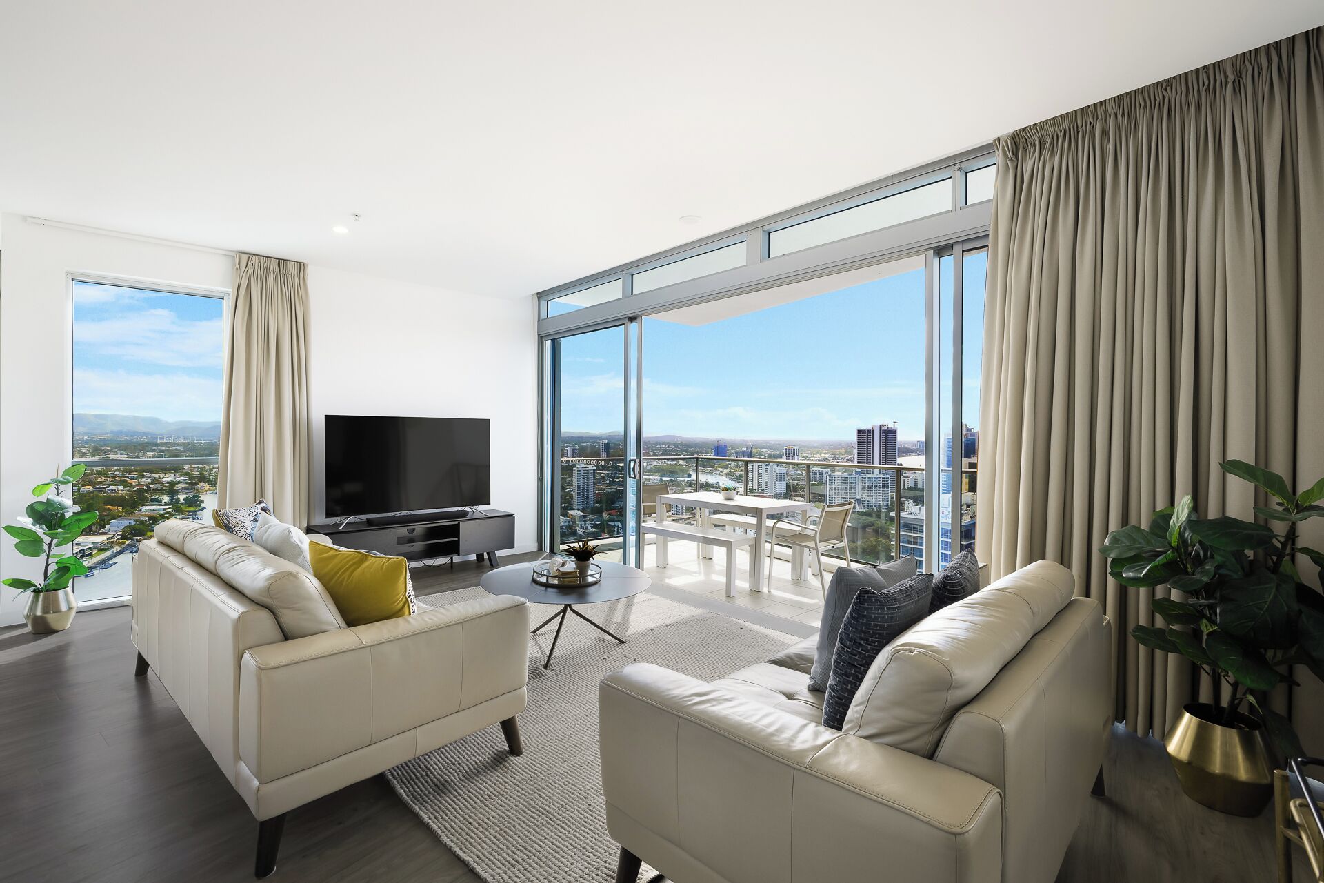 Ein modernes Wohnzimmer mit großem Fernseher, zwei Sofas, einem Couchtisch und einem Balkon mit Blick auf die Stadt.