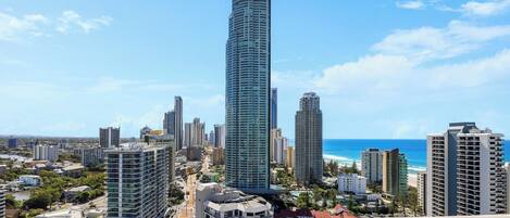 A high-rise building with a curved design, surrounded by other tall buildings and a coastline.
