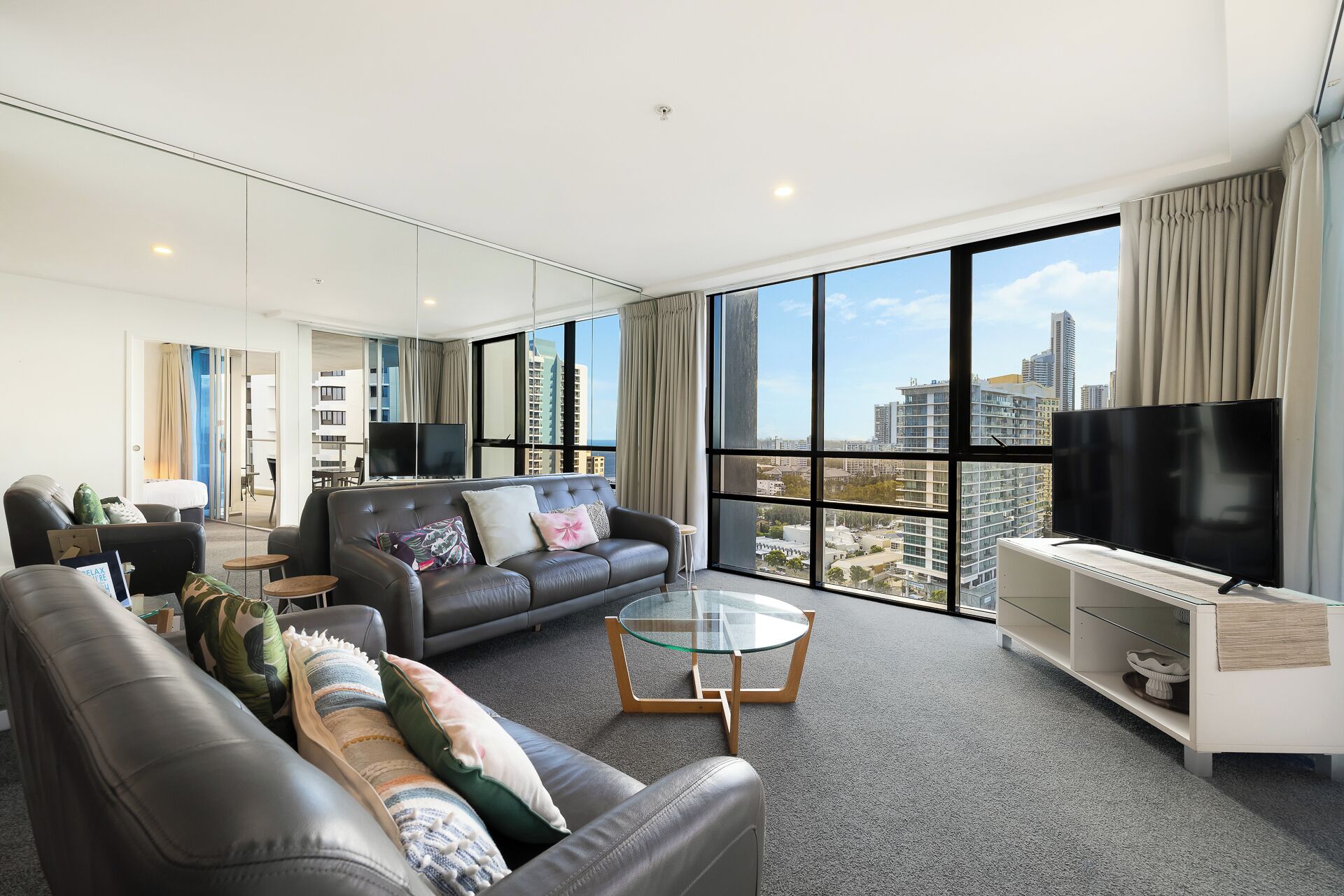 A modern living room with a leather sofa, a glass coffee table, and a flat-screen TV.