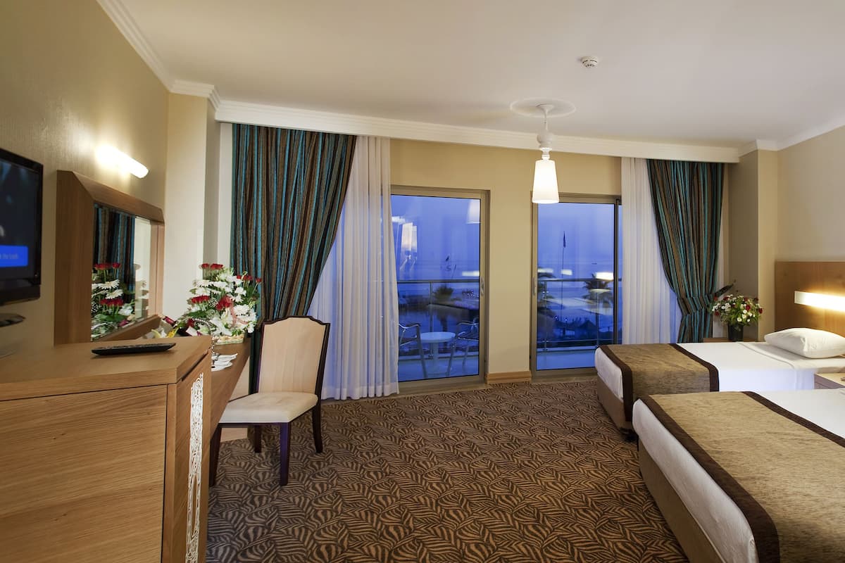 A hotel room with a bed, a desk with a TV, a chair, a desk lamp, and a view of the outside.