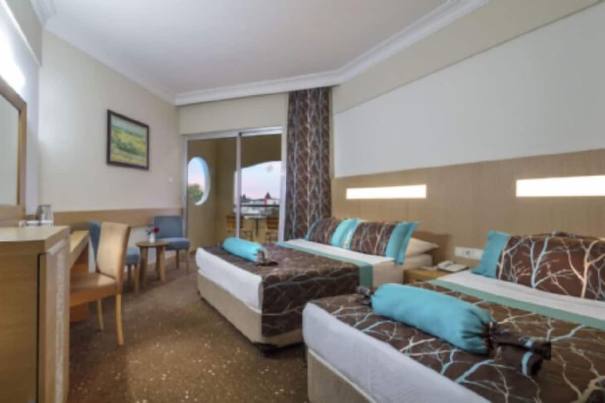 A hotel room with two beds, a desk, a television, and a view of the outside.