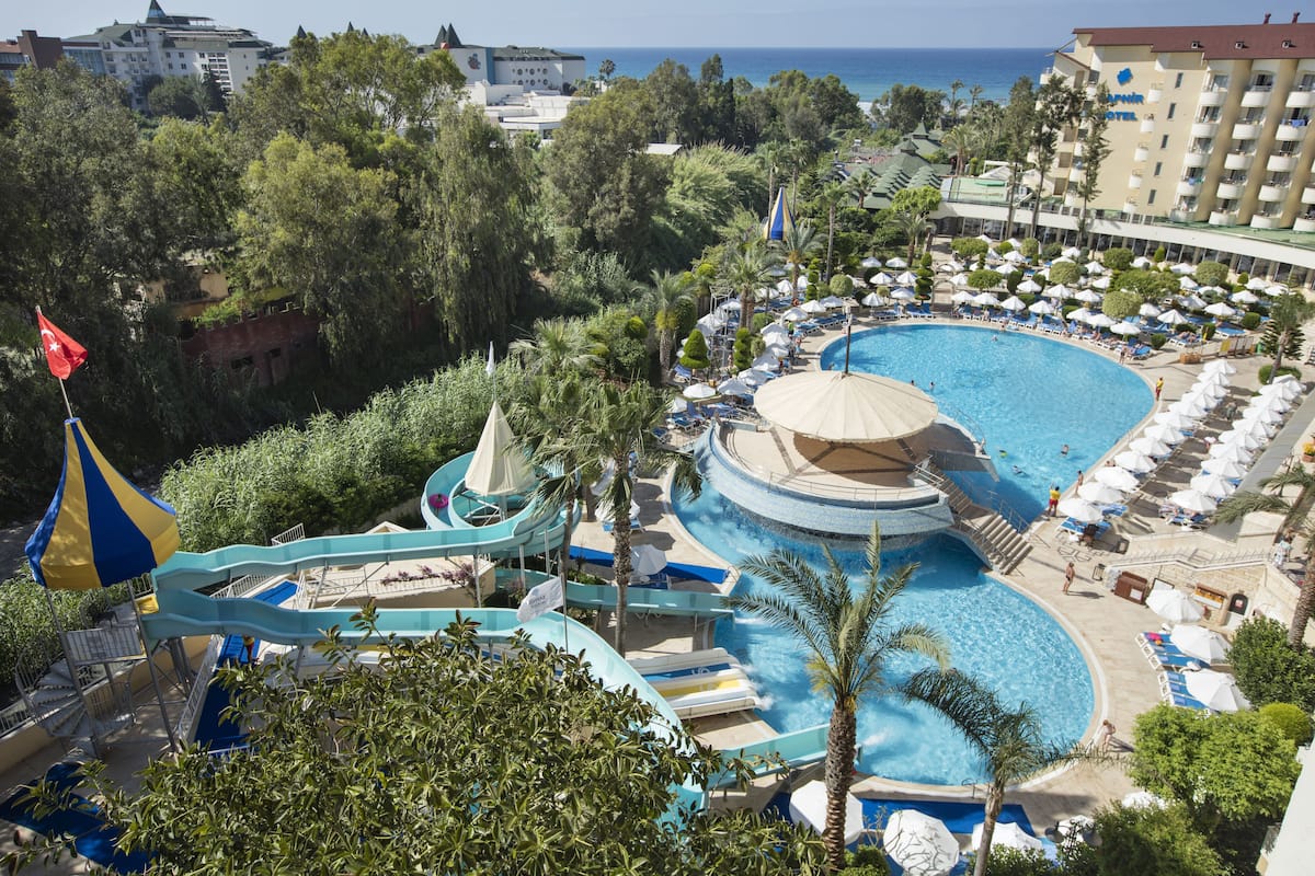 A resort with a large pool, a water slide, and a beach area with umbrellas.